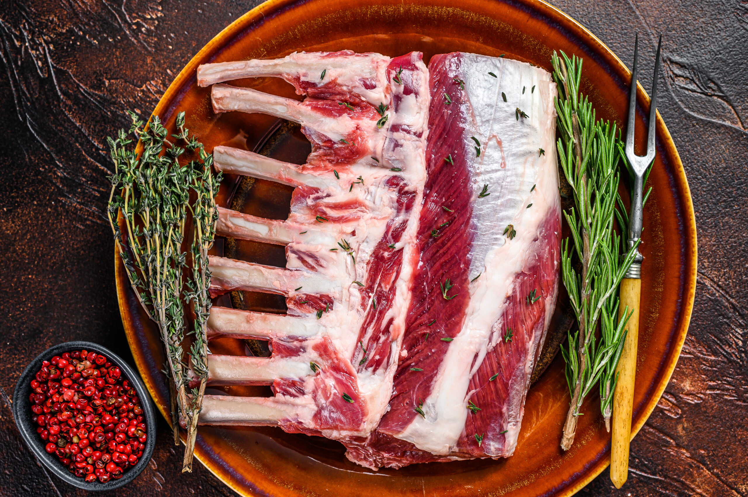 Raw fresh rack of lamb with green herbs. Dark background. Top vi