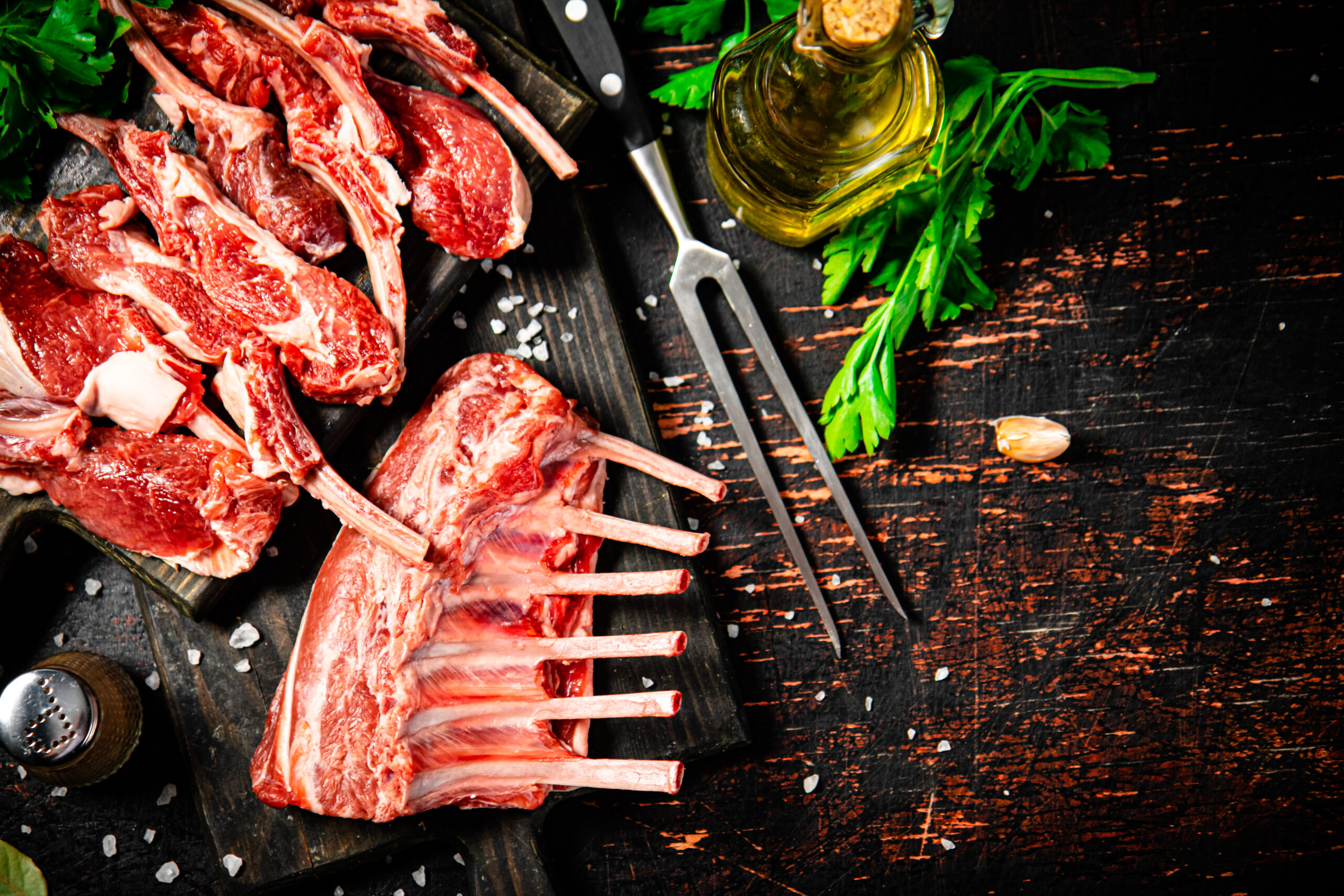 Raw rack of lamb with parsley on a cutting board.