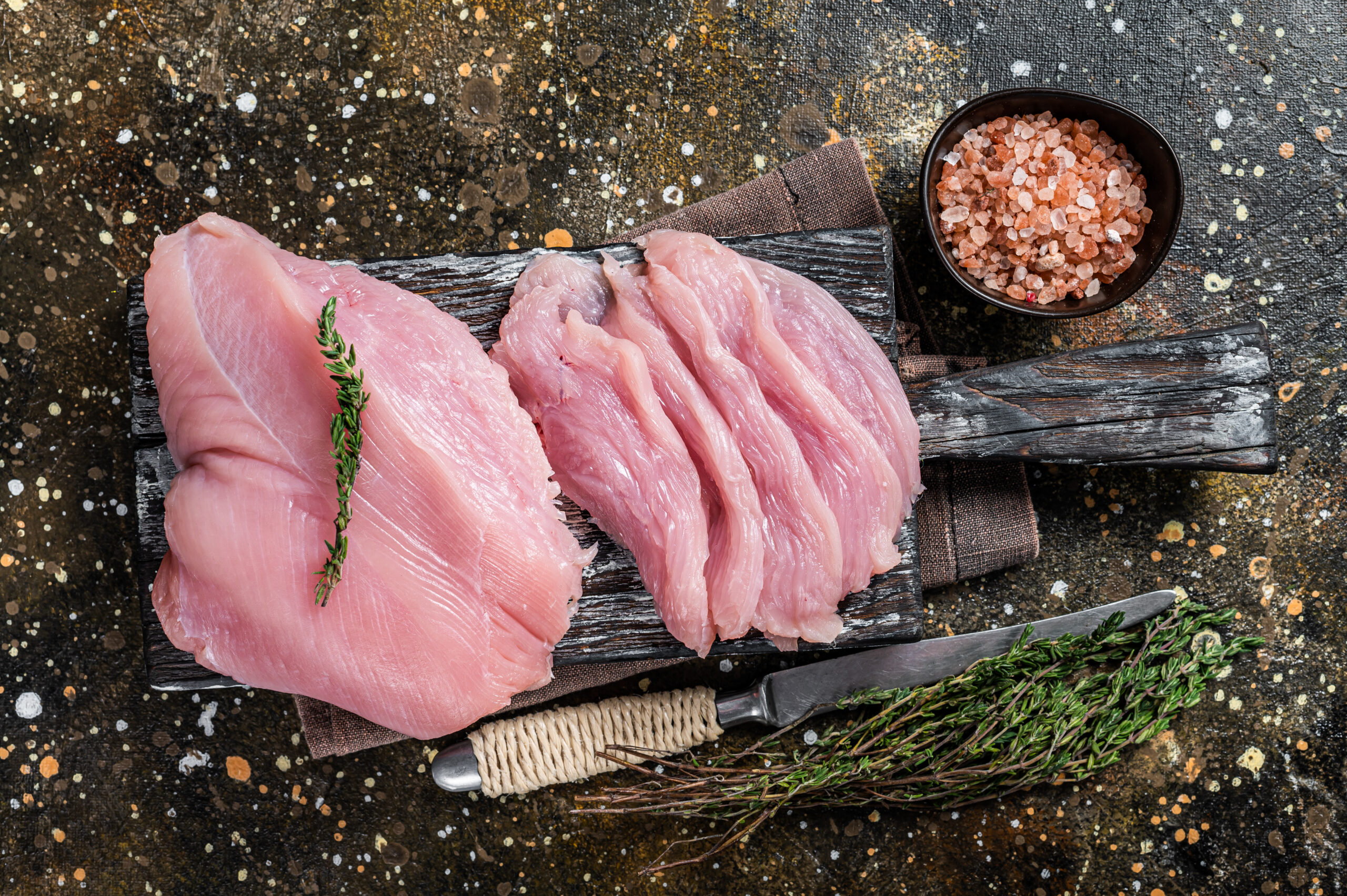 Sliced Raw turkey breast fillet meat on a cutting board with butcher knife. Brown background. Top View.